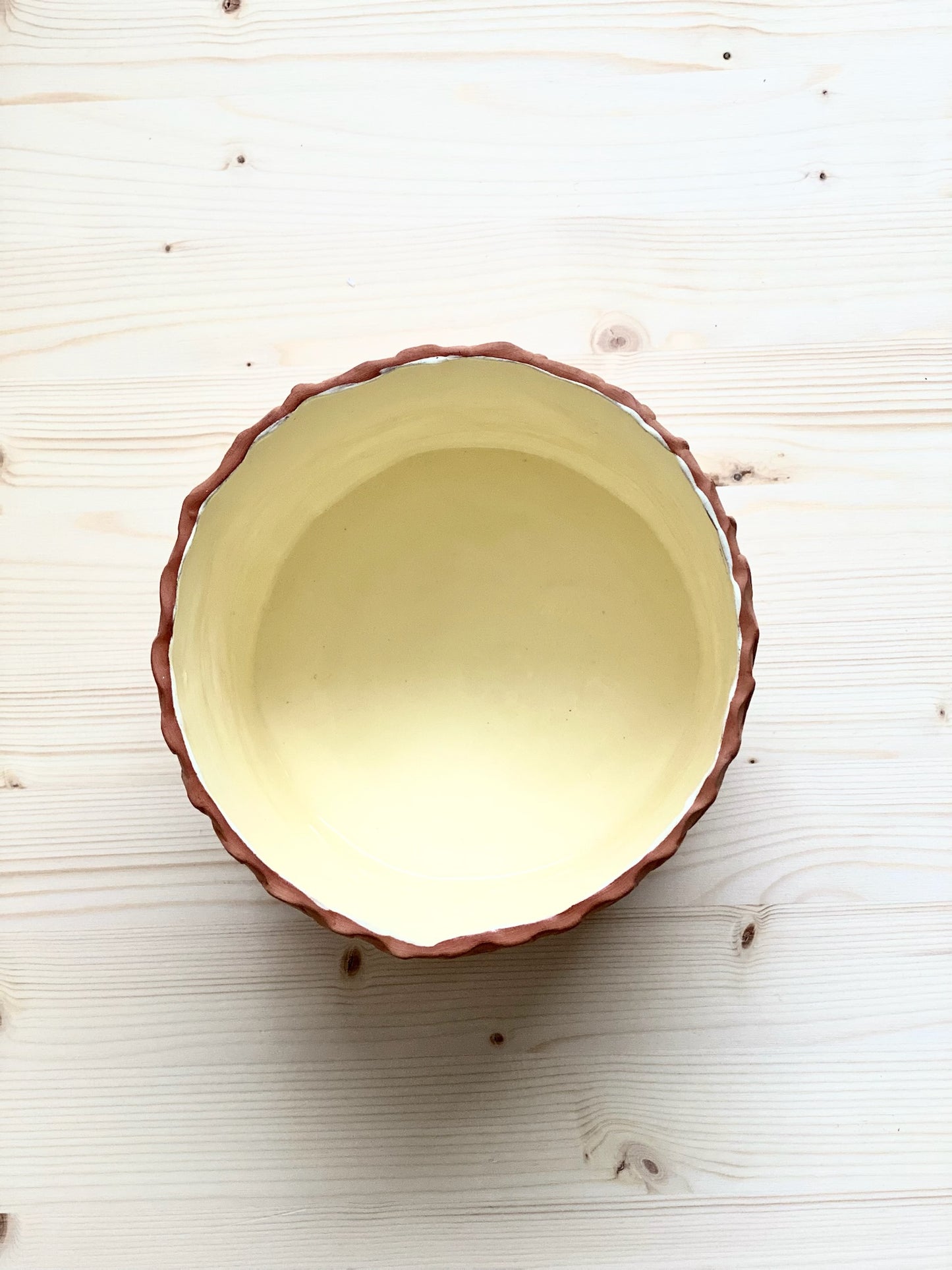 Kavlad kruka med stämplad yta. Glaserad ljusgul insida. Rå utsida